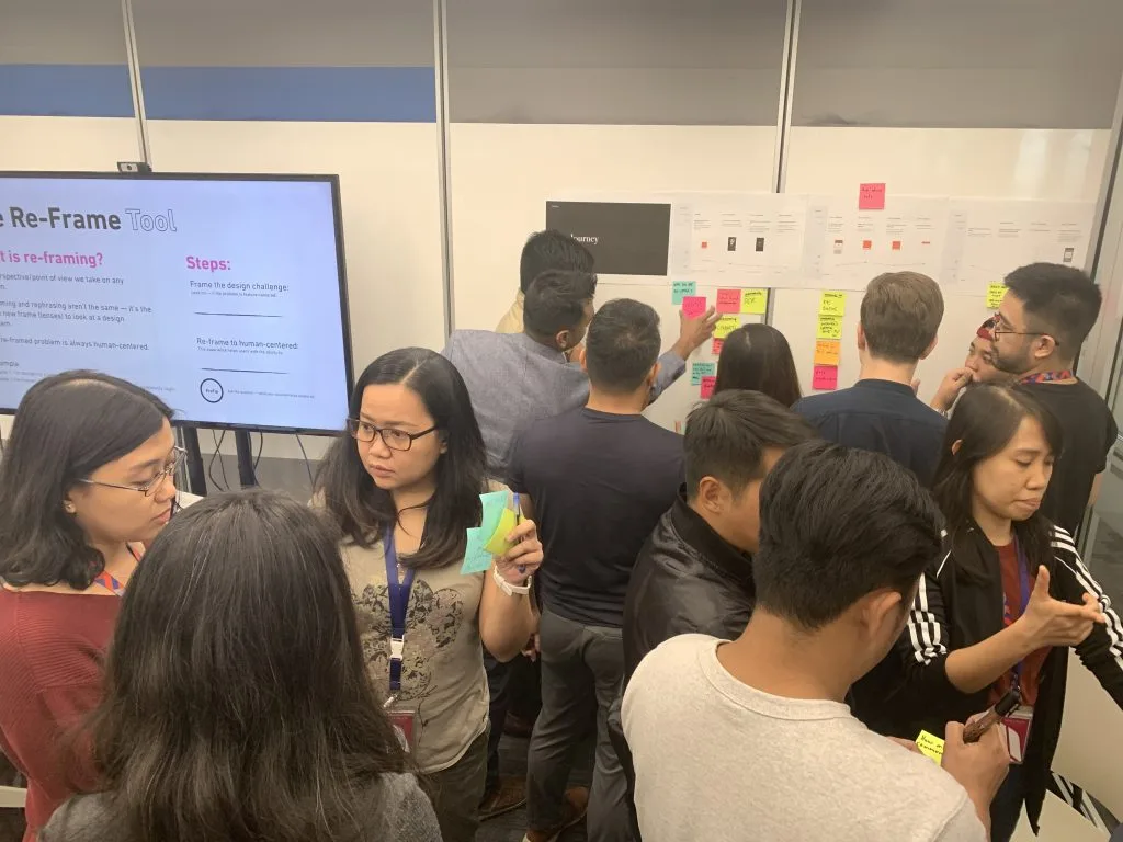 Design team gathered at a wall of sticky notes during a re-frame workshop exercise
